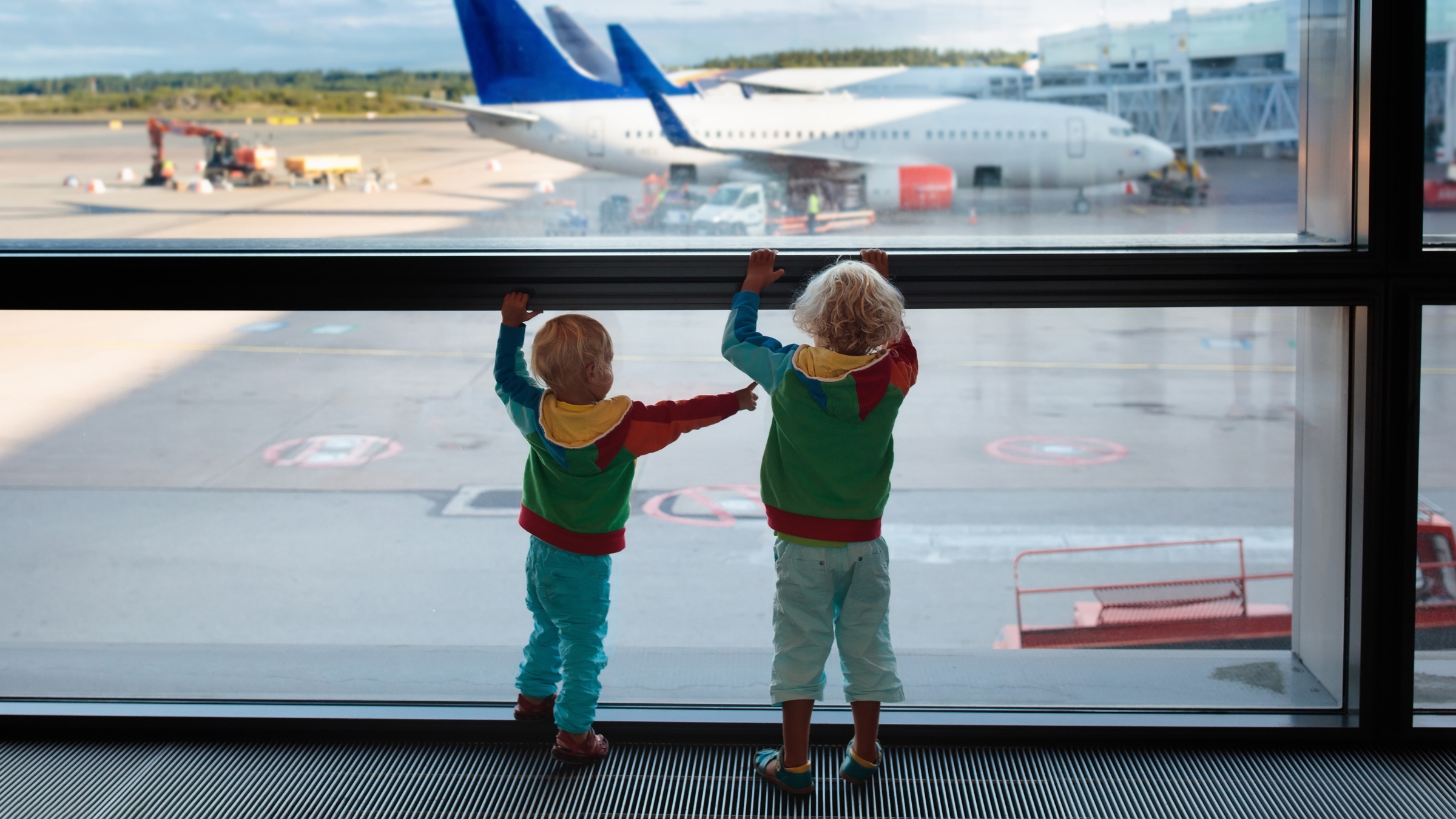 deux enfants devant l'aéroport avec avion en arrière-plan - blogue AES voyager avec des enfants